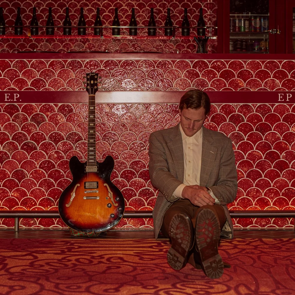Cover art for Jem Pryse's E.P., sitting at a red tiled bar with a guitar